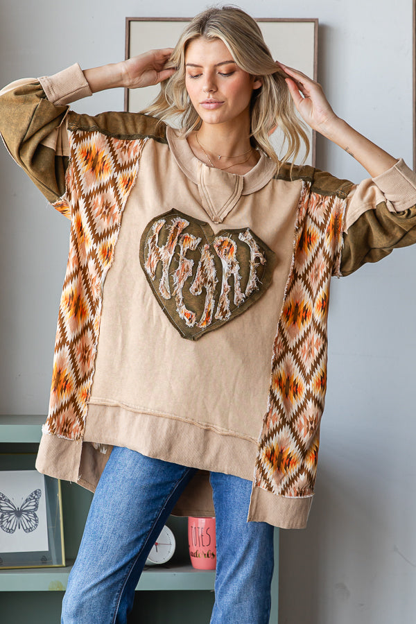 Tan heart appliqué pullover with arms raised, showing wide patterned panels and an uneven hem