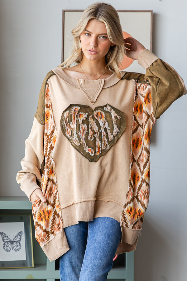 Coffee patchwork pullover with a large frayed heart, shown from the front with one hand near the neckline