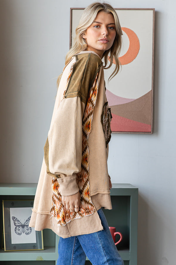 Side view of a tan pullover with olive shoulder panels, geometric patchwork and a longer back hem