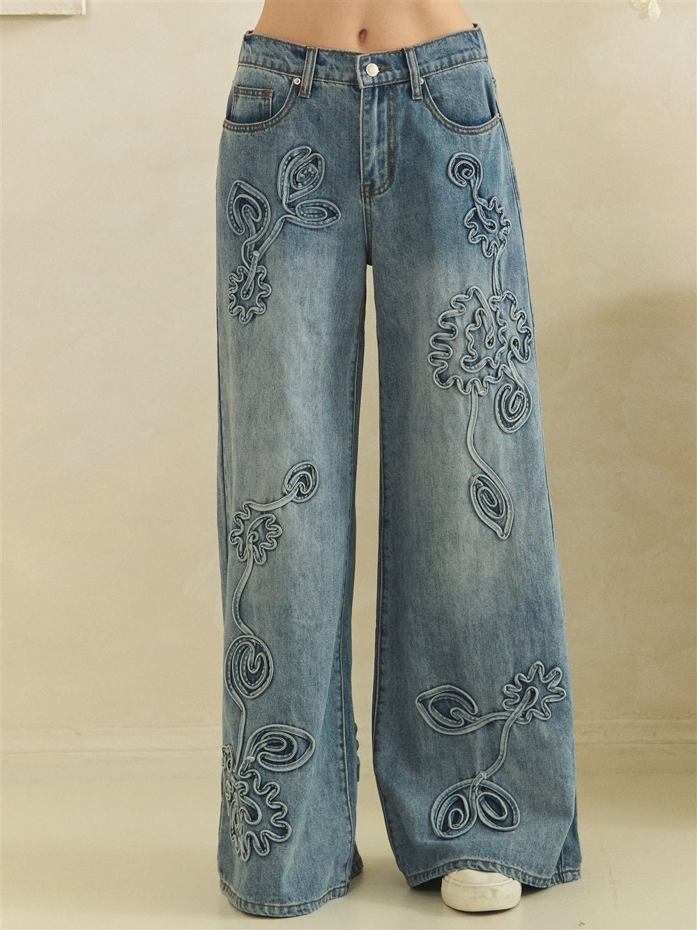 Front waist-to-hem view of blue wide-leg jeans with oversized tonal flowers and curling stems.