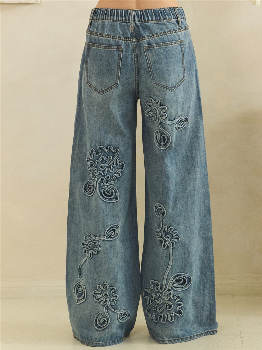 Back view of blue floral jeans showing elastic waistband, two patch pockets and full-length wide legs.