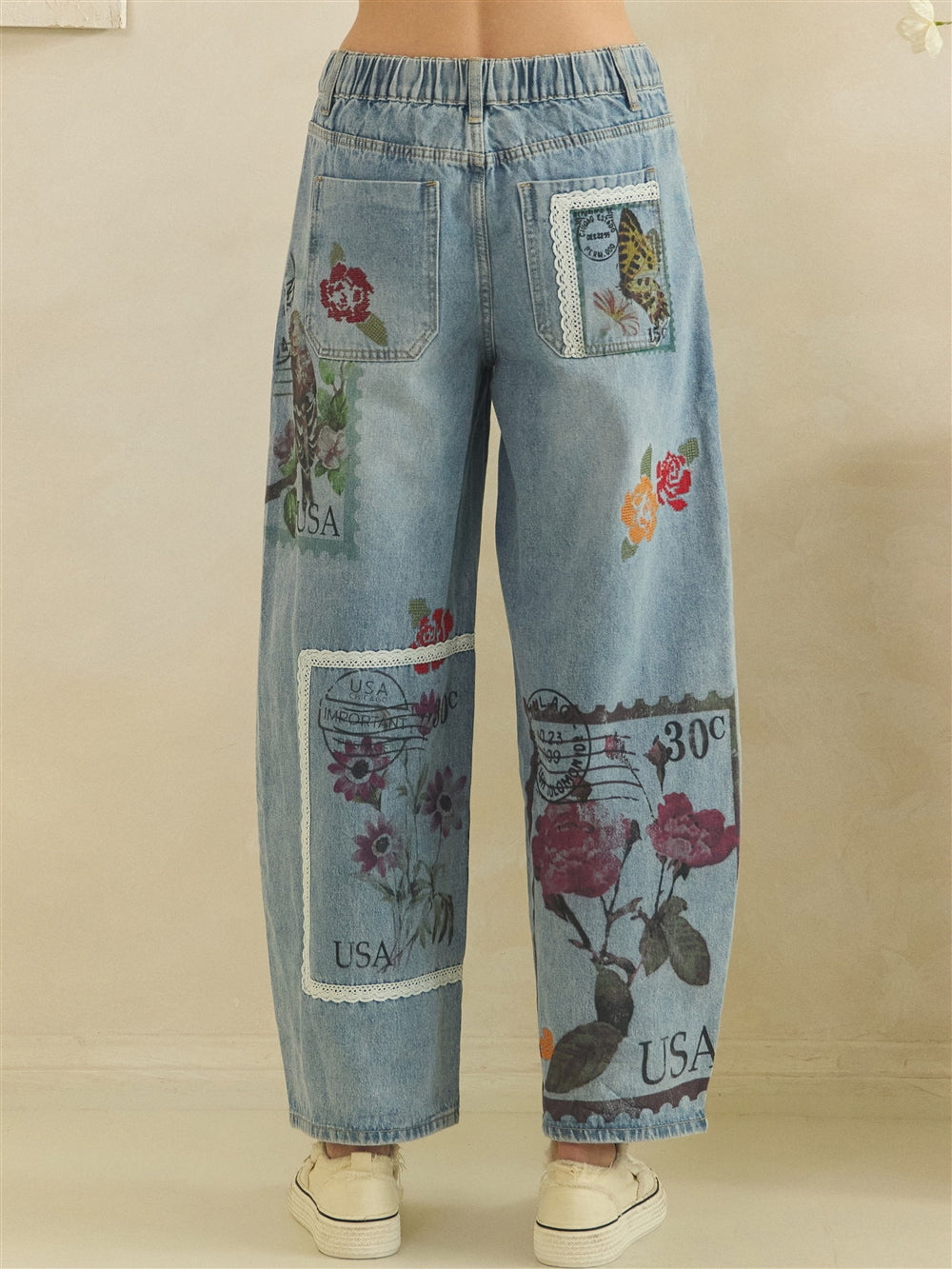 Back view of floral postage barrel jeans with an elastic waistband, patch pockets and lace-edged artwork