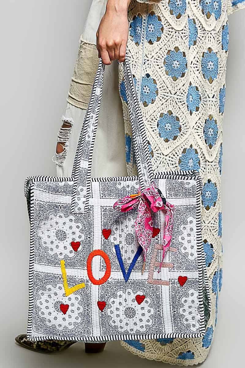 Front of a quilted paisley tote with colorful LOVE lettering and red hearts held by a model