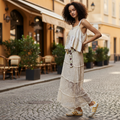 Tiered floral lace maxi skirt in Natural — front view on model in garden setting, styled with a crochet jacket and gold sneakers.