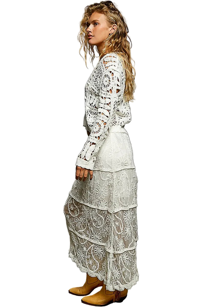 Woman wearing a white lace outfit against a gray wall.