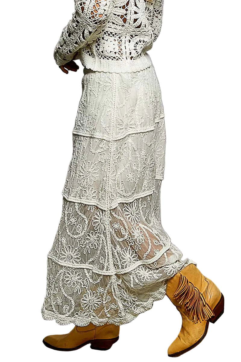 Person wearing a long, layered lace dress with yellow boots against a plain background