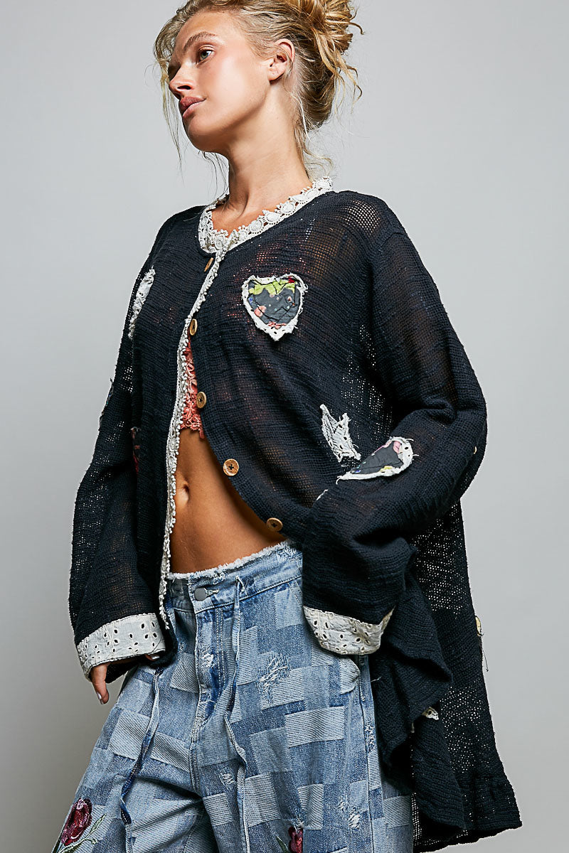 POL Clothing black open-knit cardigan showing scattered heart and star appliqués, back view on model
