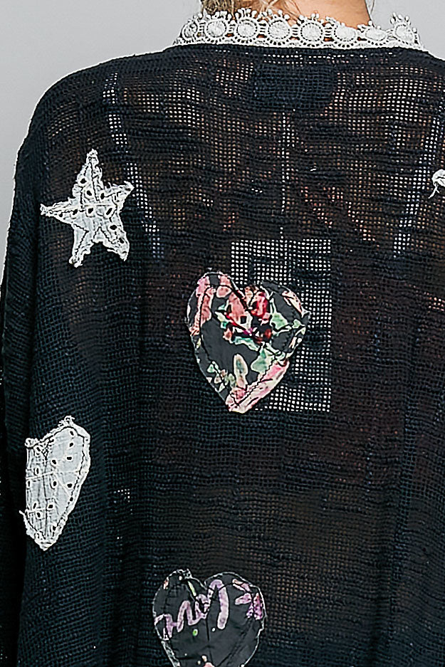 Close-up detail of POL black cardigan showing mixed floral heart appliqué patches and lace trim
