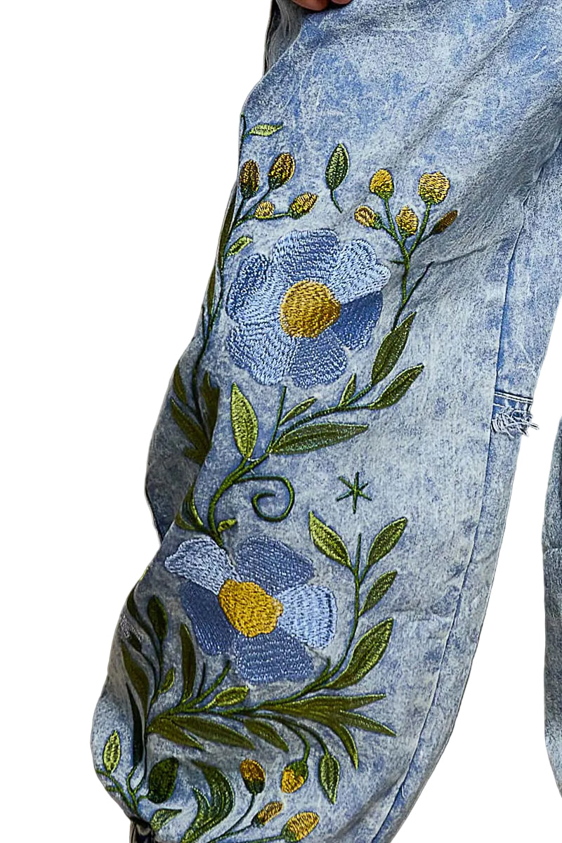 POL blue denim jogger pants, close-up detail of large floral embroidery with blue flowers and green vine on mineral wash denim
