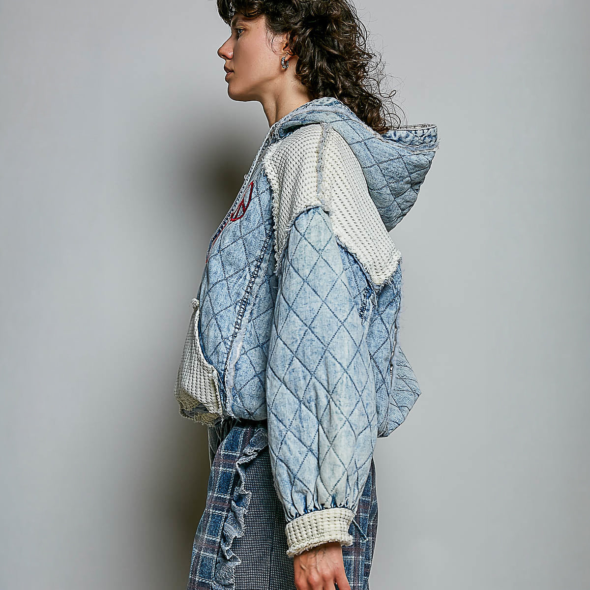 POL Clothing Denim Multi quilted hoodie on model, side view showing cream waffle-knit sleeve and adjustable hem drawstring
