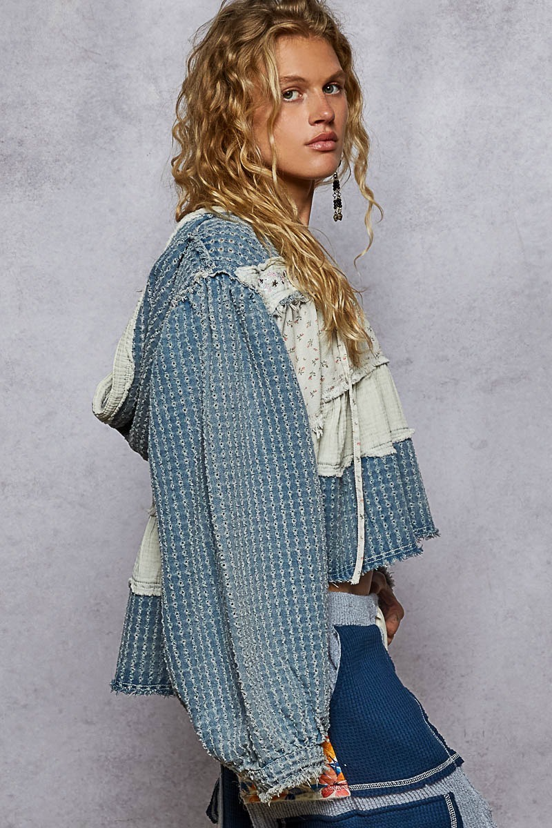 Side view of a denim-blue patchwork hoodie showing a full sleeve, raw edges and a longer back hem.