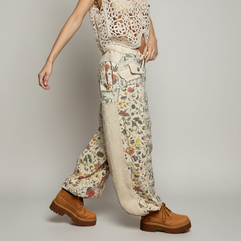 Person wearing floral-patterned pants with a textured top and brown boots against a gray background