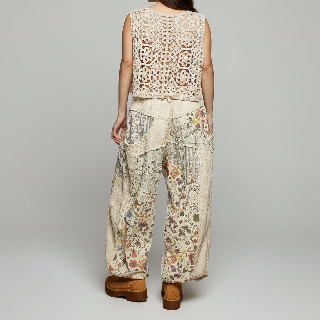 Person wearing a floral and patchwork patterned outfit with wide-leg pants against a gray wall.