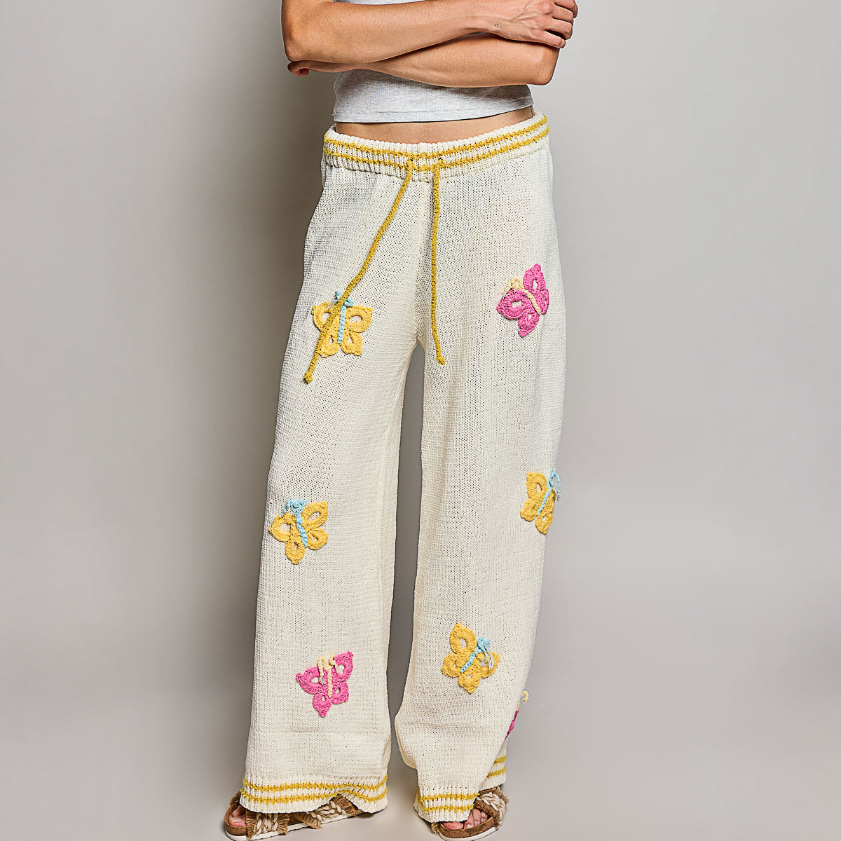 POL Clothing cream multi knit pants front crop view showing yellow drawstring waistband and crochet butterfly appliques
