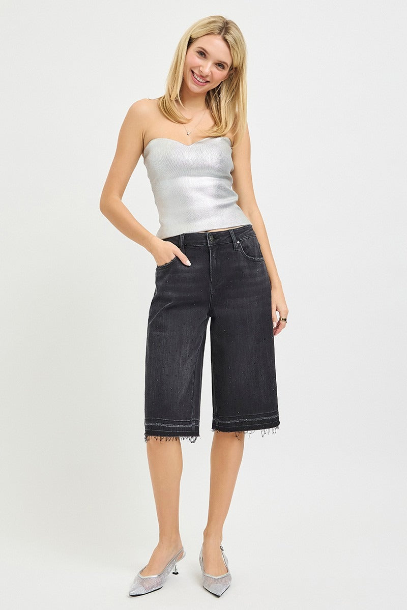 Woman wearing a silver strapless top and black denim shorts on a white background