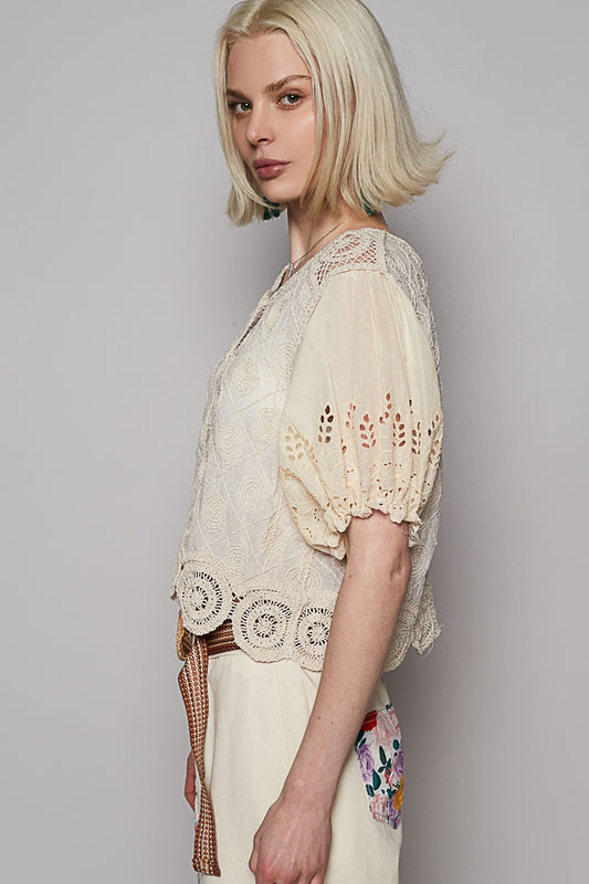 Woman wearing a light-colored lace top against a plain background