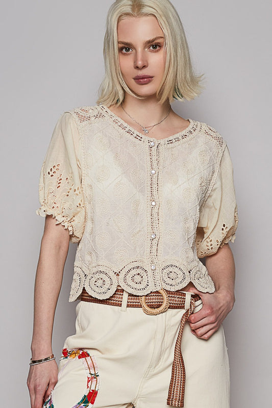 Woman wearing a cream-colored lace top and pants against a plain background