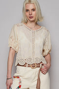 Woman wearing a cream-colored lace top and pants against a plain background