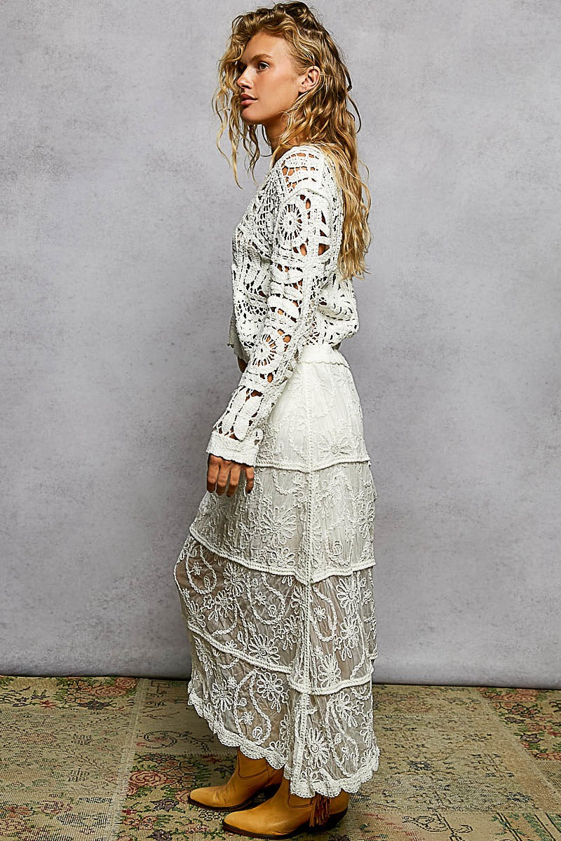 Woman wearing a white lace outfit against a gray wall.