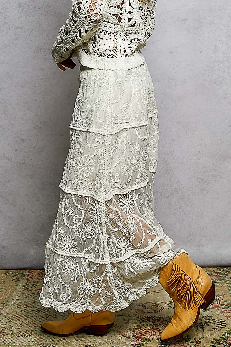 Person wearing a long, layered lace dress with yellow boots against a plain background