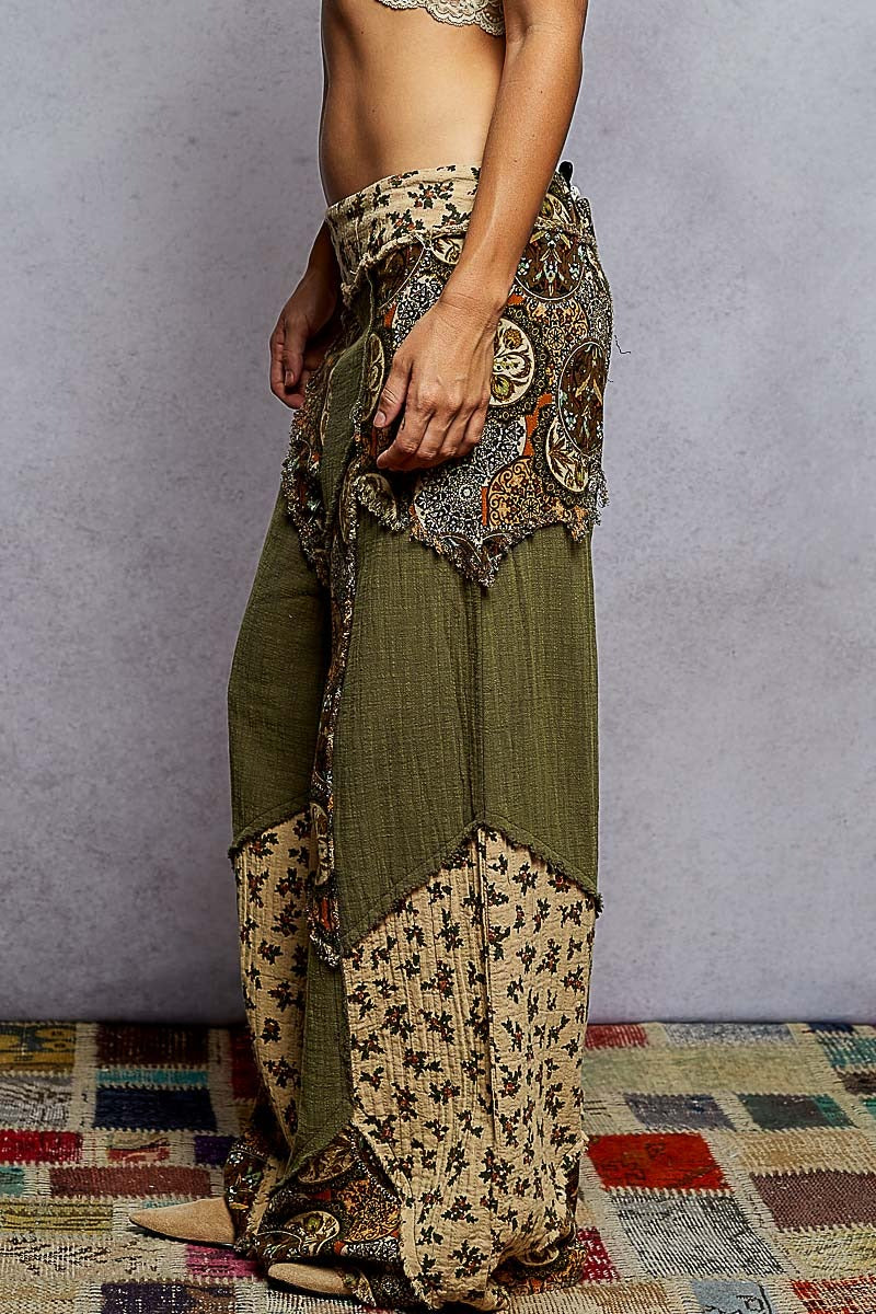 Person wearing a patterned skirt and green pants on a textured floor.