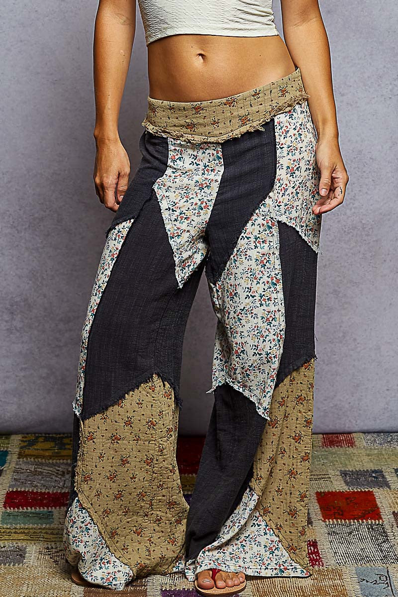 Person wearing a unique, layered outfit with floral and patterned pants on a textured rug.
