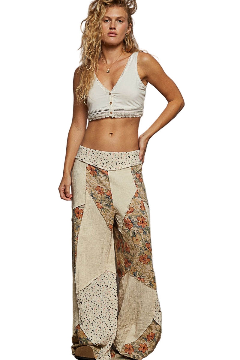Woman wearing a white crop top and floral patchwork pants against a plain background