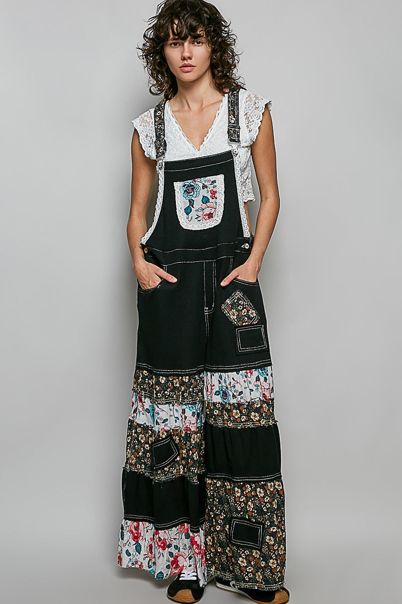 Woman wearing a black patchwork overalls with floral patterns on a plain background