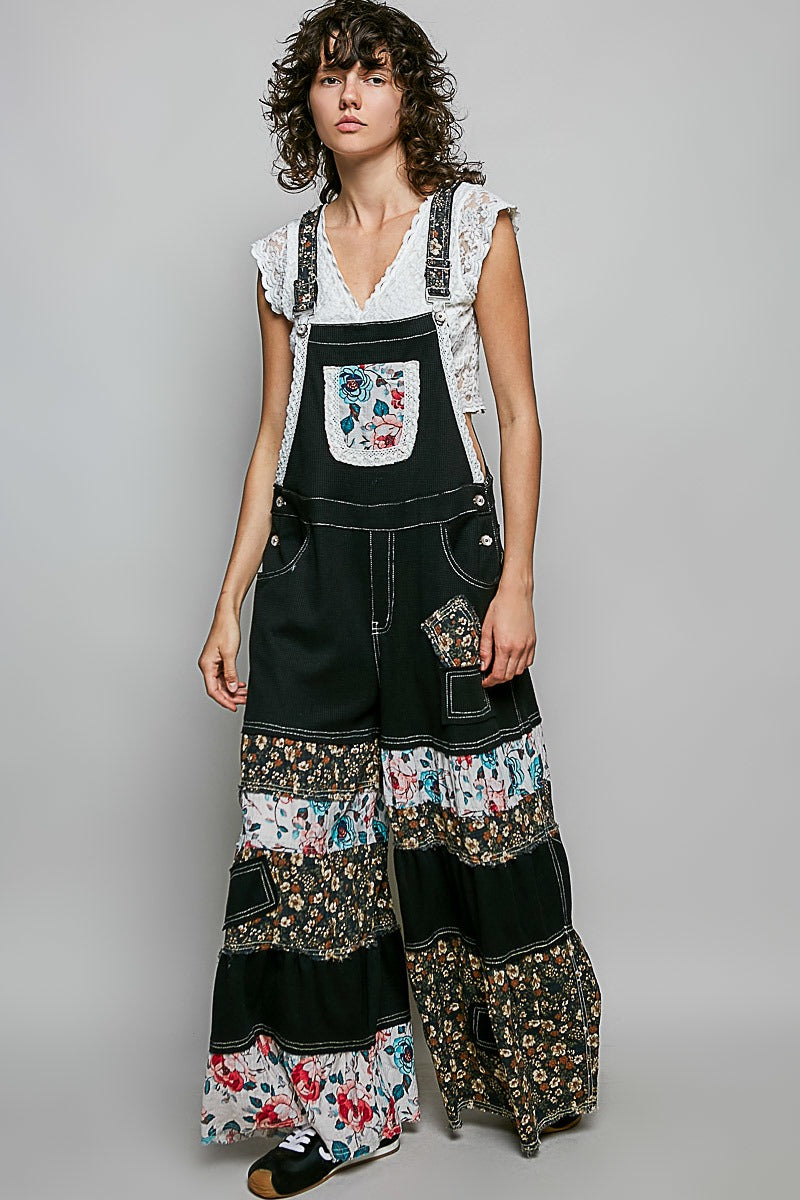 Person wearing a black denim overall with floral patchwork design on a plain background