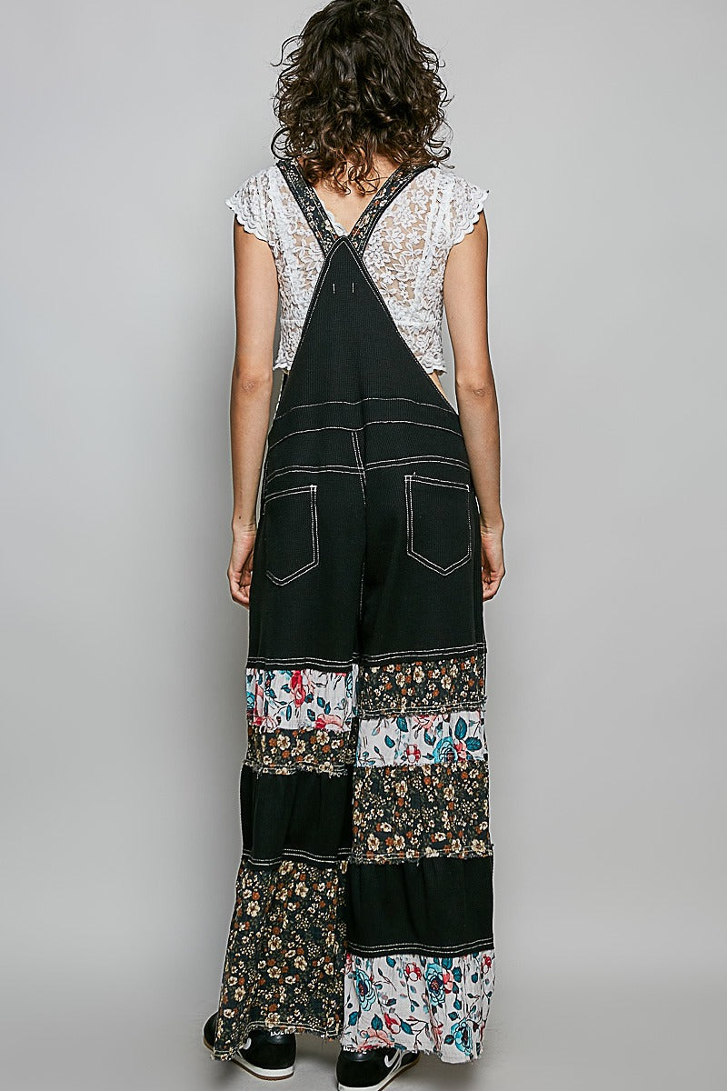 Person wearing a black patchwork overalls with floral patterns on a plain background