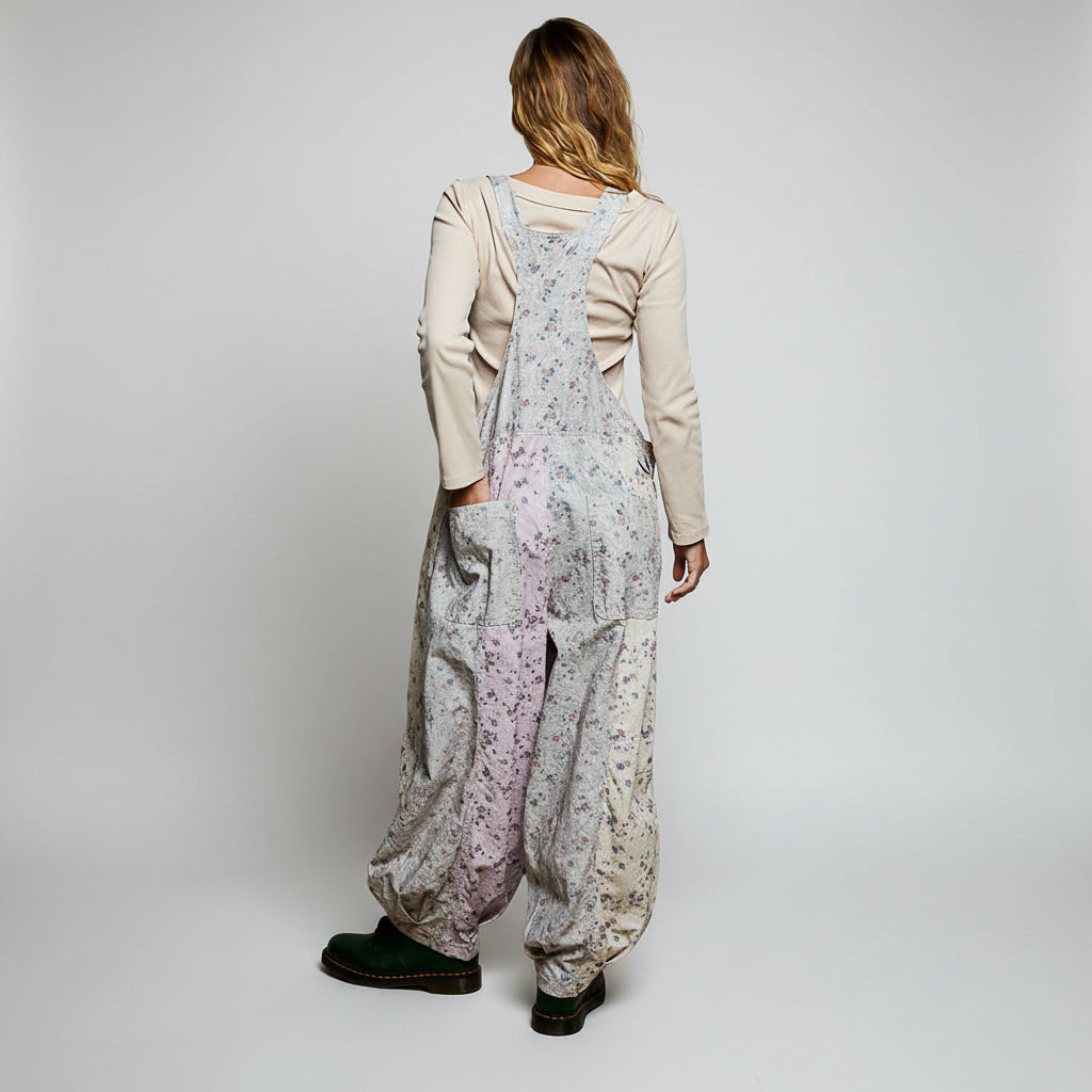 A woman shown from the back wearing loose, wide-leg floral overalls over a light beige long-sleeve top and black shoes, against a plain white background.