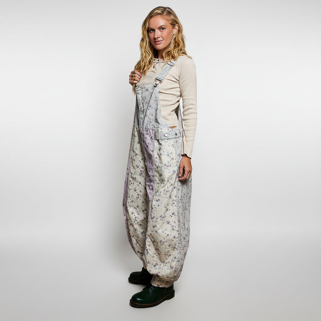 A woman modeling a pair of loose-fitting floral print overalls over a cream long-sleeve top and dark green boots, photographed against a solid white background.
