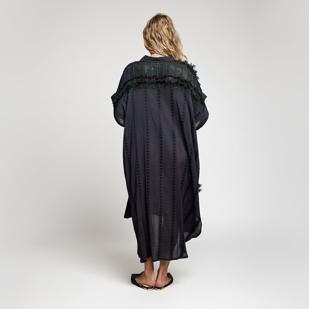 Person wearing a long black dress with a textured top on a white background