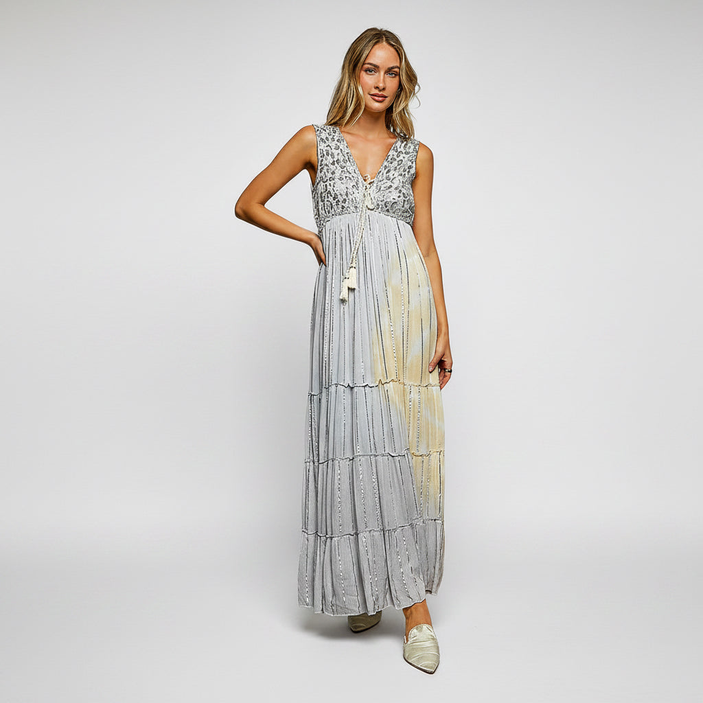 A woman modeling a sleeveless, tiered maxi dress with a light gray and white floral lace bodice and a flowing, semi-sheer skirt that fades to a pale yellow-gold at the hem, set against a plain white background.