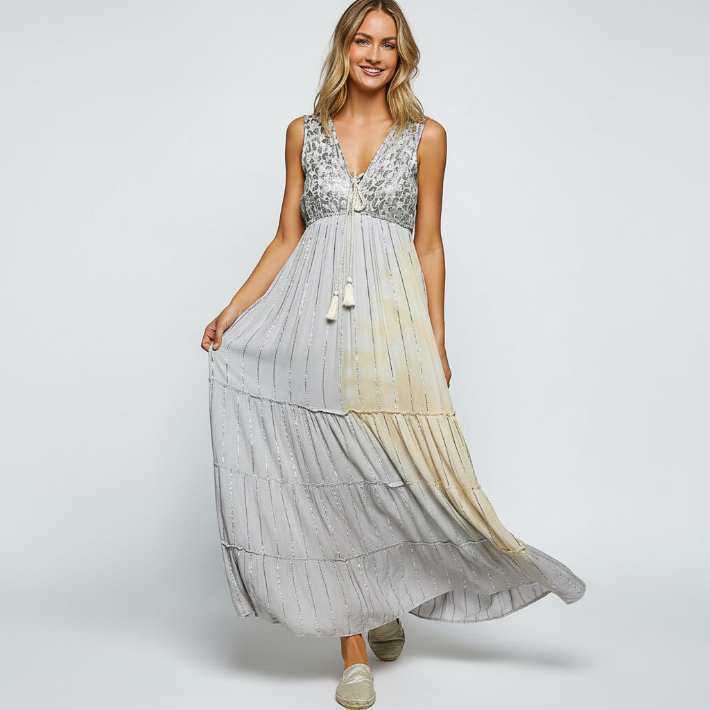 A woman modeling a sleeveless maxi dress with a gray floral lace bodice and a tiered skirt that fades from gray to pale yellow, standing against a textured gray wall.