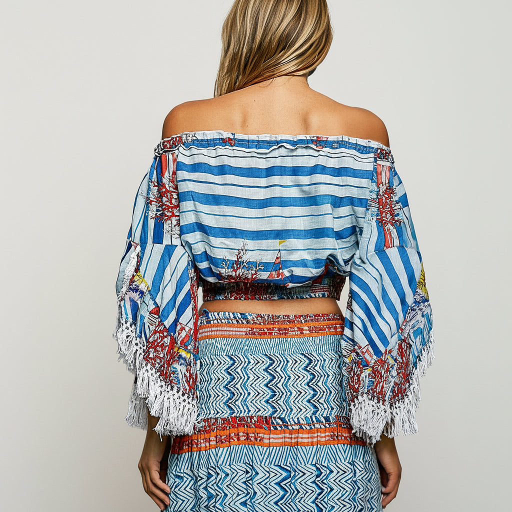 A woman shown from the back wearing a blue and white striped off-the-shoulder crop top with colorful embroidered details and white fringe, paired with a matching patterned skirt against a plain white background.