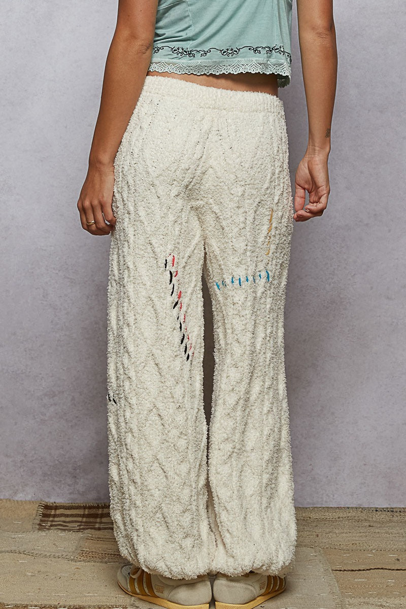 Person wearing cream-colored pants with textural pattern against a plain background