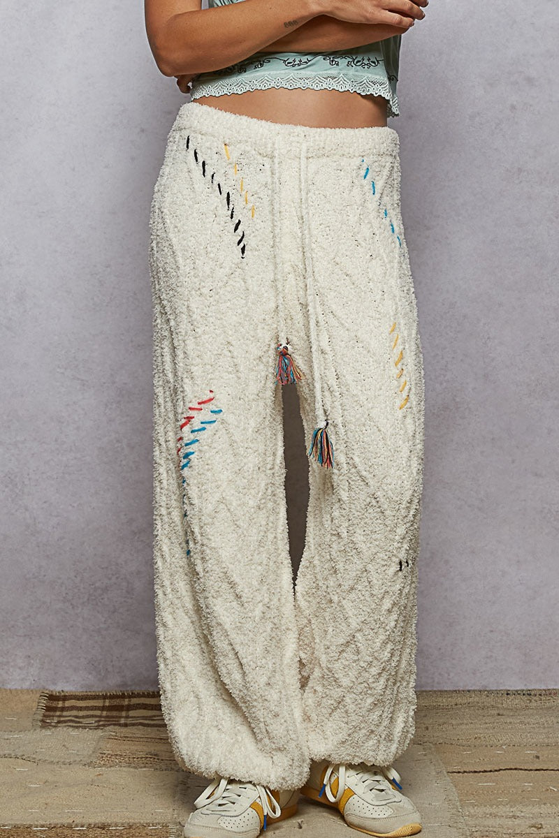 Person wearing cream-colored pants with colorful tassels against a plain background