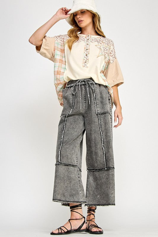 Woman wearing a beige top with lace details, plaid shirt, and wide-leg denim pants on a white background