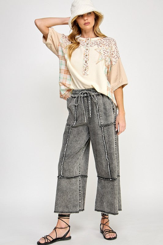 Woman wearing a beige lace top and gray wide-leg pants on a white background