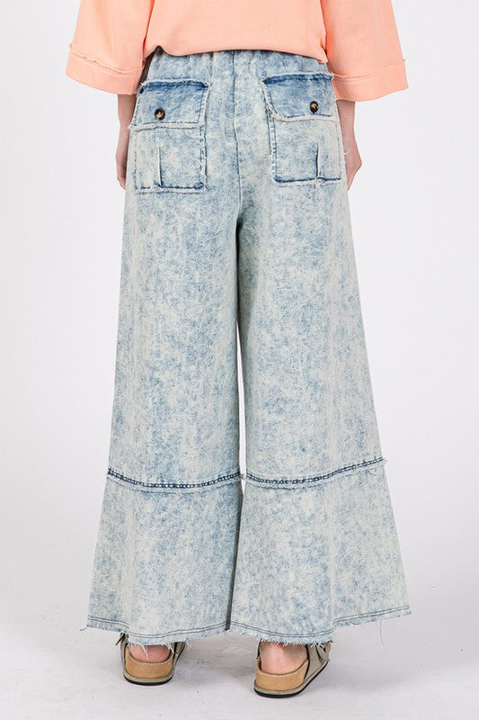 Light blue acid-wash wide-leg jeans worn by a person on a white background