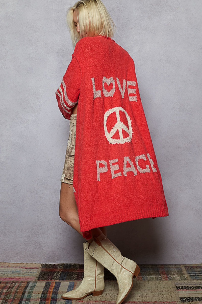 Person wearing a red cardigan with 'Love Peace' text against a gray wall.