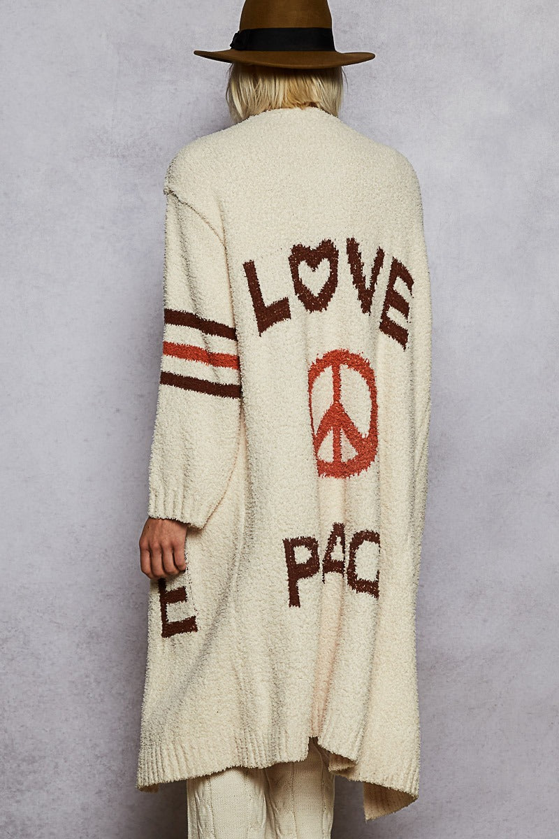 Person wearing a long cream cardigan with 'LOVE PEACE' text on a plain background