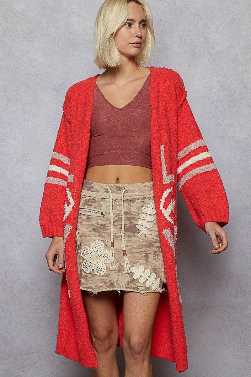 Woman wearing a red cardigan, brown top, and beige skirt with floral embroidery on a gray background