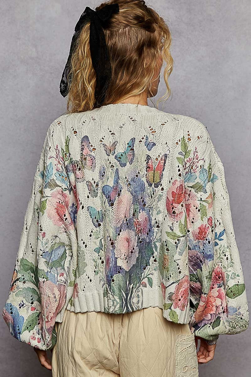 Person wearing a floral and butterfly patterned cardigan against a gray background