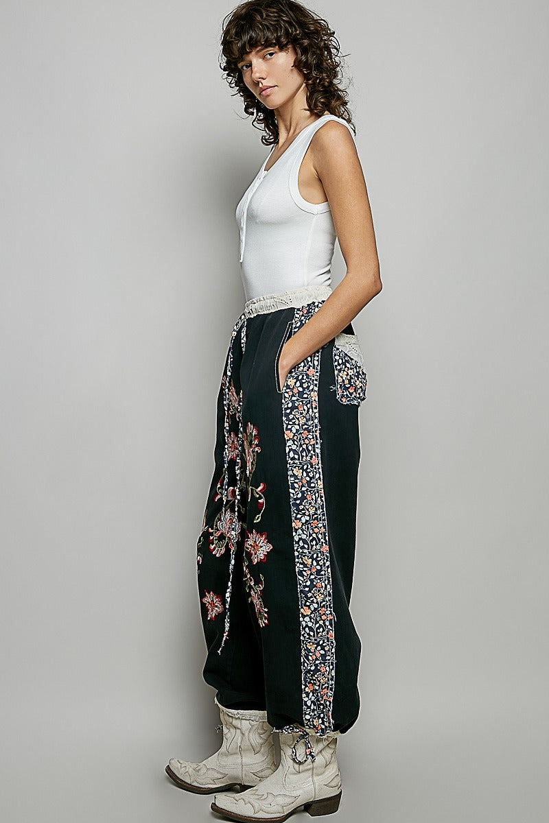 Woman wearing a white tank top and black floral pants against a gray background