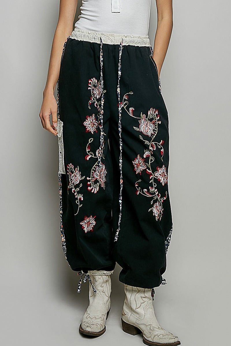 Person wearing black pants with floral embroidery and white boots on a plain background