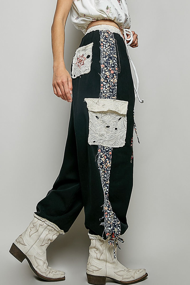 Person wearing black pants with floral embroidery and white cowboy boots on a plain background