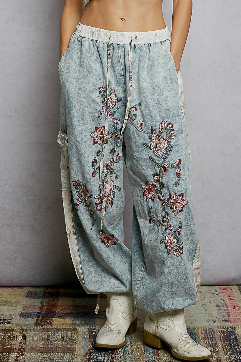 Light blue denim pants with floral embroidery worn by a person on a patterned rug.