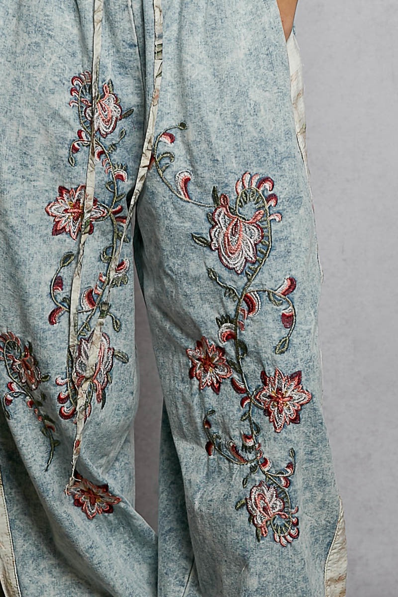 Light blue pants with intricate floral embroidery on a gray background